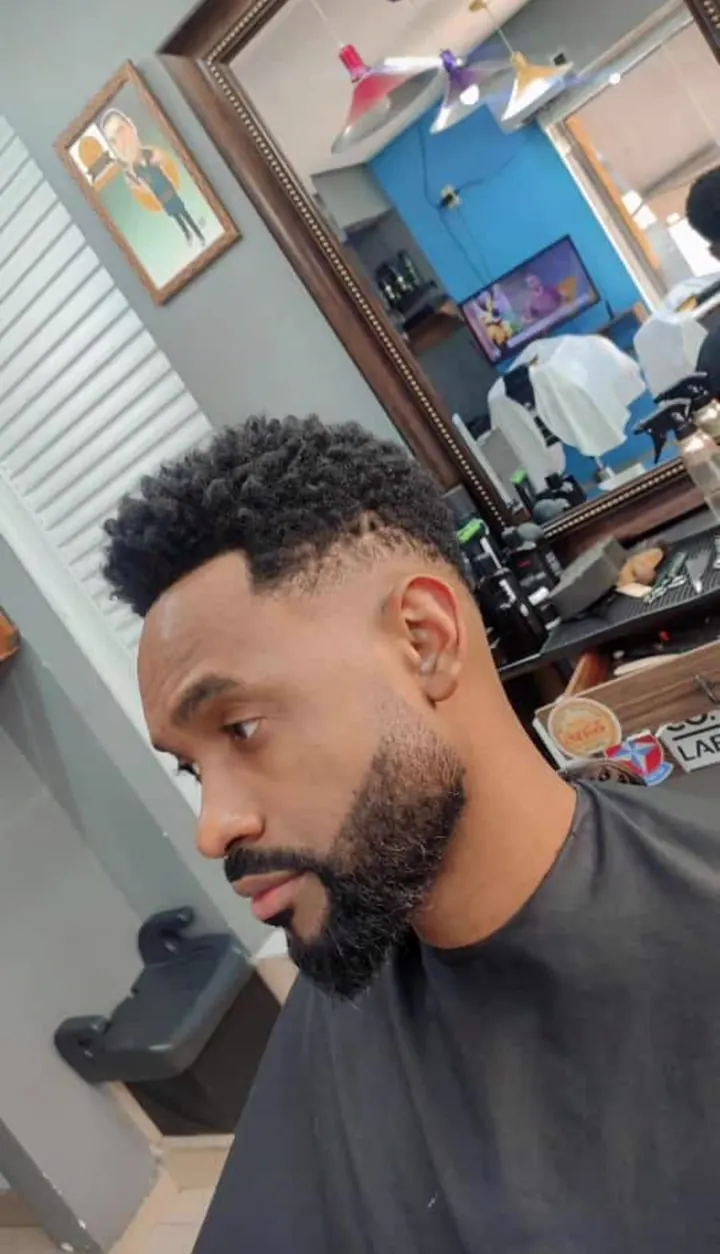Cliente de perfil com a barba cheia desenhada e degradê nas laterais.