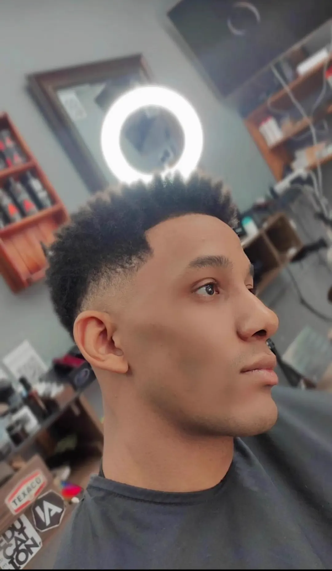 Cliente de perfil na cadeira, com degradê baixo nas laterais e topo crespo volumoso.